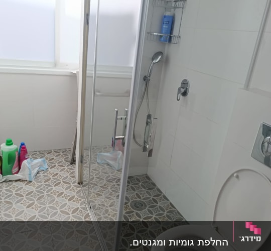 מקלחון עם ראש מקלחת וחומרי ניקוי על הרצפה